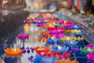 Fototapeta na wymiar Close up view, lotus flower candles with flame among floating colourful flower on water for worship buddha in Thai temple. Pray for buddha in traditional Asian culture. 