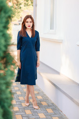 Fototapeta na wymiar Red-haired model in a dark blue dress posing in the garden.