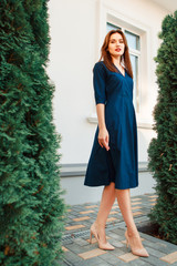 Red-haired model in a dark blue dress posing in the garden.