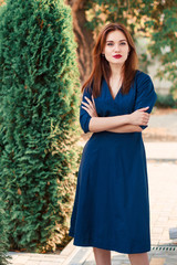 Red-haired model in a dark blue dress posing in the garden.