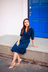 Obraz premium Red-haired model posing at the blue door in a dark blue dress