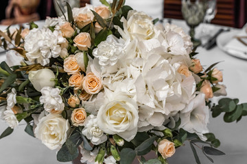 The bride's bouquet of white and yellow flowers on wedding arrangement in restaurant. Beautiful bridal bouquet of white and yellow peonies and roses on the table in the restaurant