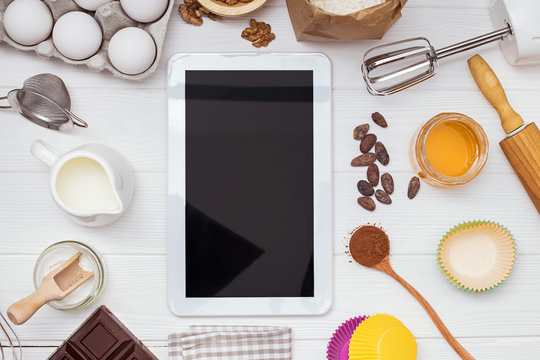 Ingredients and tools for baking and tablet with blank screen and place for text or image on white table