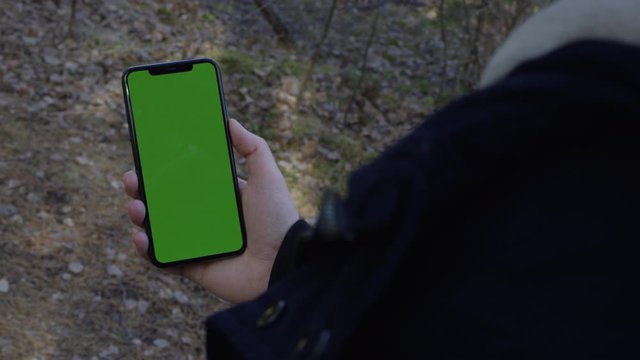 Hand holding a modern smartphone in the woods with chroma key green screen