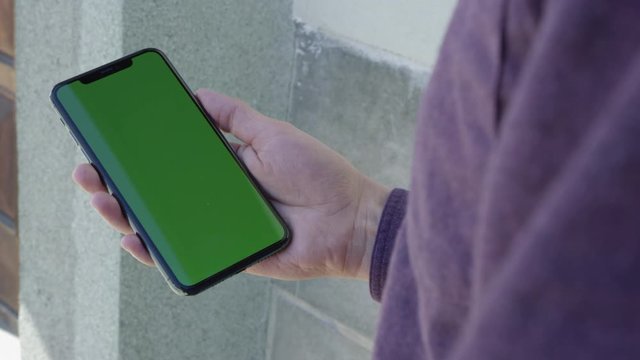 Hand holding a smartphone mobile device outside with chroma key green screen