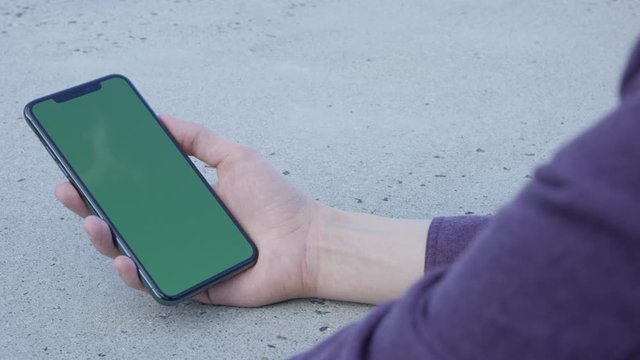 Hand holding phone using mobile device in urban setting with green screen