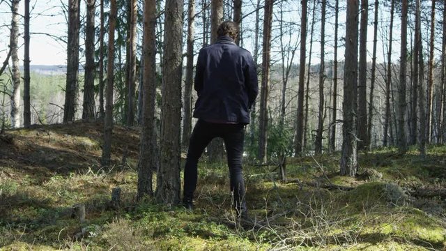 Man urinates next to a tree in the forest in public