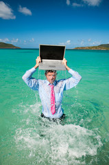 Businessman splashing out of the water with a laptop balanced on his head in bright blue tropical sea