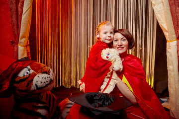 Fototapeta premium Family during a stylized theatrical circus photo shoot in a beautiful red location. Models mother and daughter posing on stage with curtain