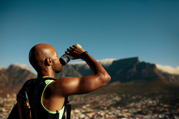Obraz premium Athlete drinking water after morning run on mountain