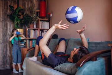 Young boy in sportswear playing with volleyball ball in living room at home, lifestyle during...
