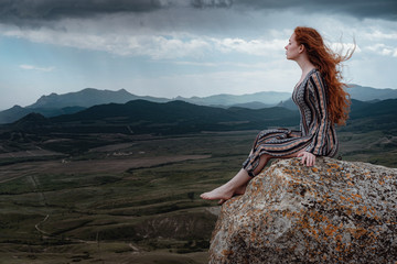 Ginger woman sits on a cliff and looks at an impending storm