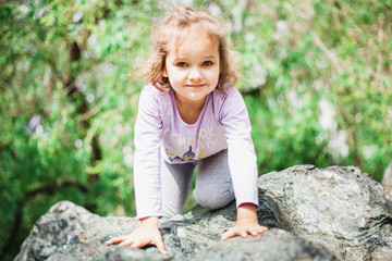 A little girl in a t-shirt and pants climbs on rocks, mountains, peaks, conquering peaks, game, Park, forest, adventure with family, learning geography, terrain