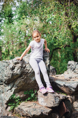 Naklejka na ściany i meble A little girl in a t-shirt and pants climbs on rocks, mountains, peaks, conquering peaks, game, Park, forest, adventure with family, learning geography, terrain