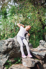 A little girl in a t-shirt and pants climbs on rocks, mountains, peaks, conquering peaks, game, Park, forest, adventure with family, learning geography, terrain