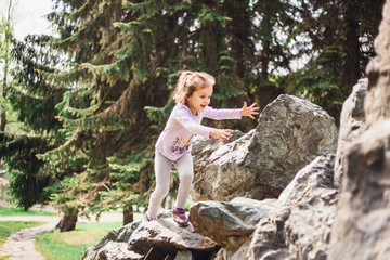 A little girl in a t-shirt and pants climbs on rocks, mountains, peaks, conquering peaks, game, Park, forest, adventure with family, learning geography, terrain