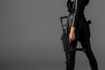 cropped view of futuristic african american woman posing with assault rifle on grey - obrazy, fototapety, plakaty