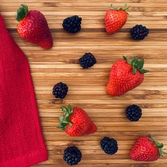 Strawberries and blackberries on a wooden kitchen counter. Ingredients for baking a summer berry, strawberry and blackberry, pie or tart. Top down flat lay view. Red and summery food flat lay