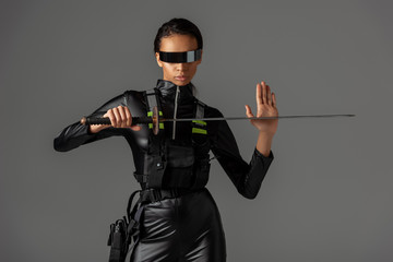attractive futuristic african american woman in glasses with sword isolated on grey
