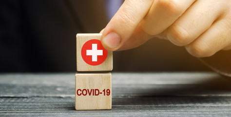 A man holds a block with a medical cross and the inscription Covid-19. Coronavirus pandemic infection. Healthcare, medicine concept. Health insurance. Ambulance. Quarantine, lockdown