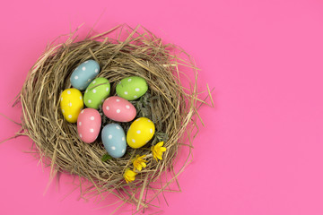 Colored Easter eggs in a nest on a pink background, top view