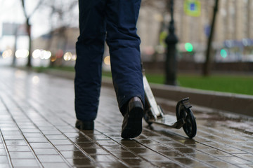 Rain in the spring Moscow. Puddles at the street. Girl riding push scooter. Coronavirus pandemic lifestyles.