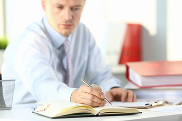 Male arm in suit and tie hold silver pen filling schedule in notepad at office workplace closeup. Legal law consult assistance gesture or finance investment advisor clerk job information gesture