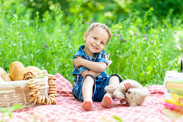 A little cute boy sits on a plaid and plays with his teddy bear.