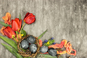 Composition of violet Easter eggs in a nest and flowers on grey background, top view, copy space