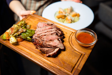 Freshly prepared meat steak sliced into pieces on a wooden board.