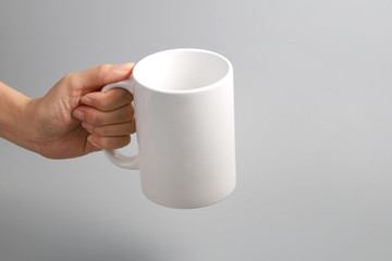 Hands holding a white mug of coffee or tea on grey background.