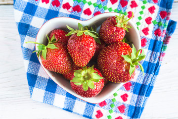 Ripe strawberries in bowl shape heart on checkered napkin top view