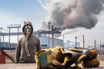 Bad ecology. Man in the old model gas masks stands againts smoking pipes metallurgical plant in...