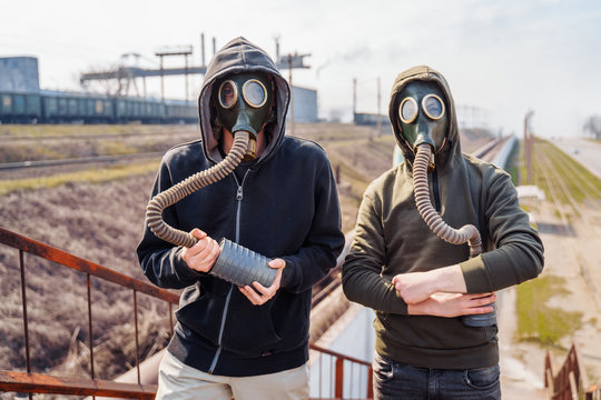 Bad ecology. Two men friends in the old model gas masks stand againts the background of a smoking metallurgical plant and look at each other. People trying to escape from ecological catastrophy