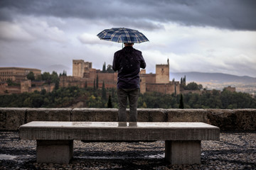 Tourist with umbrellas looking at the Alhambra from the Mirador de San Nicolas, a rainy day.