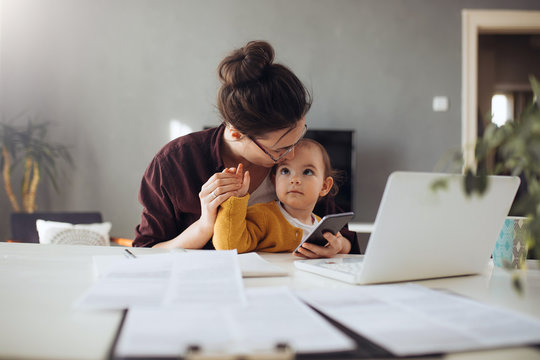 Young businesswoman working from home. Young mother using her mobile phone at her home office. She working with her child.