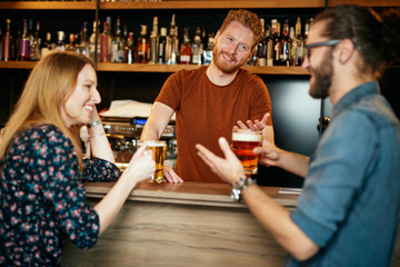 Handsome Caucasian bearded ginger standing in bar with his female friend, drinking beer, chatting and having fun. Pub interior. Nightlife.