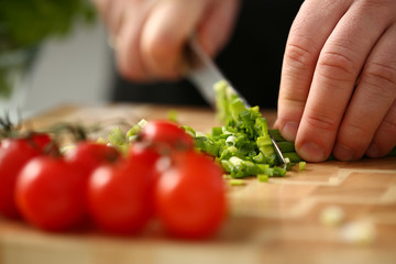 Cook holds knife in hand and cuts on cutting board green onions for salad or fresh vegetable soup with vitamins. Raw food and vegetarian recipe book in modern society popular concept.