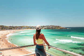 Woman at Bondi Beach, Sydney, Australia. Girl in work out gear looking at view of the ocean, sun, sea and sand scene, while on vacation. Holiday, tropical, fitness concepts.  - obrazy, fototapety, plakaty