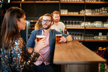 Group of friends drinking beer, chatting and having good time at pub. Night out.