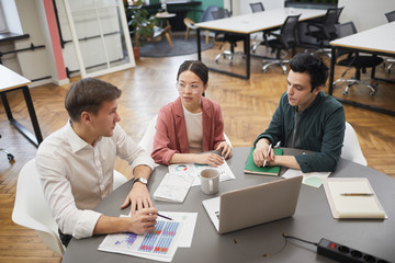 Team of young business people planning work together while sitting at the table with financial documents and laptop during meeting