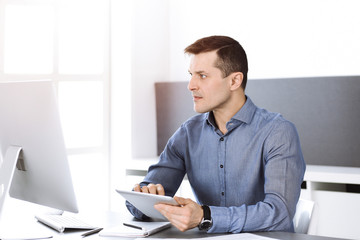 Businessman working with computer in modern sunny office. Headshot of male entrepreneur or company director at workplace. Business concept