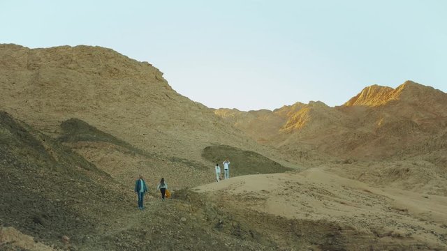 Group of tourist walk along the rock canyon in hot desert, tourists take picture and have fun. Desert mountains background, Egypt, Sinai, slow motion, full hd