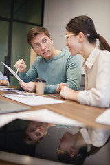 Young businessman pointing at document and talking to the young businesswoman at the table at office