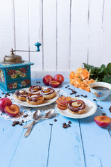 gebackene Blätterteigrosen mit Pflaumen und Puderzucker auf  hellen blauen Brettern aus Holz im nostalgischen Stil wie früher bei Oma