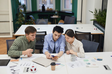 Group of creative designers examining colored patterns and working over new fashion collection at meeting at office