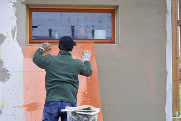 Worker fixing and covering with construction glue fiberglass reinforcing mesh on rigid polyurethane...