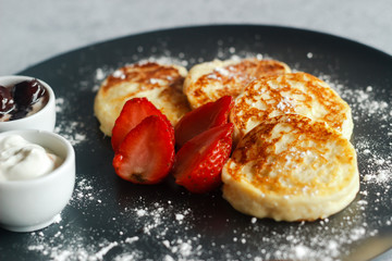 Tasty cheese pancakes with strawberries, sour cream and cherry jam. Cheese pancakes on a plate