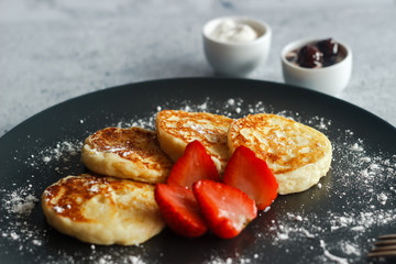 Tasty cheese pancakes with strawberries, sour cream and cherry jam. Cheese pancakes on a plate