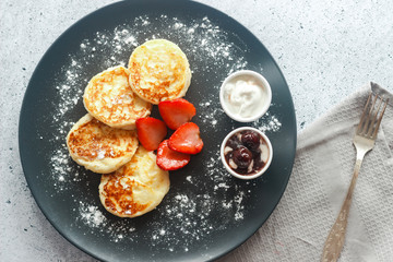 Tasty cheese pancakes with strawberries, sour cream and cherry jam. Cheese pancakes on a plate